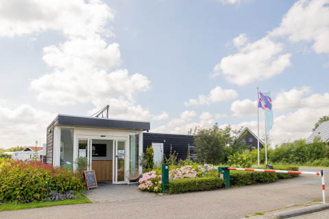 Eingang zu Camping Natuurlijk de Veenhoop - Safaritenten Friesland mit Blumen und Flaggen am Weg.