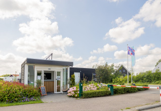 Entrance of Camping Natuurlijk de Veenhoop - Safaritenten Friesland with flowers and flags by the road.