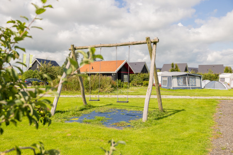 Speelplein met schommels op Camping Natuurlijk de Veenhoop - Safaritenten Friesland, met tenten en hutten.