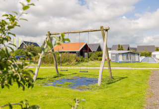 Speelplaats met schommels op Camping Natuurlijk de Veenhoop - Safaritenten Friesland, met tenten en huisjes.