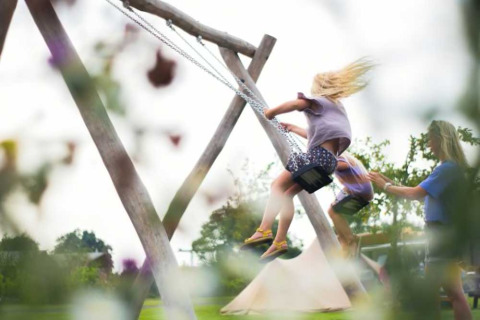 Children playing on swings at Camping Natuurlijk de Veenhoop safari tents campsite in lush surroundings.