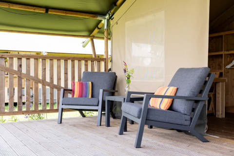 Zwei bequeme Stühle mit bunten Kissen auf einer Holzveranda im Camping Natuurlijk de Veenhoop, Safaritenten Friesland.