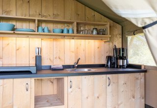 Moderne houten keuken in een safaritent bij Camping Natuurlijk de Veenhoop met servies en apparaten.