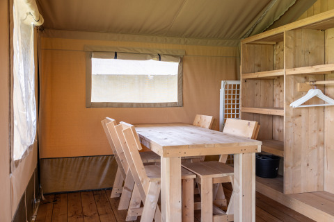 Interieur van een glamping safaritent met houten tafel, stoelen en kast bij Camping Natuurlijk de Veenhoop.