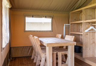 Binnenzicht van een glamping safaritent met houten tafel, stoelen en rekken bij Camping Natuurlijk de Veenhoop.