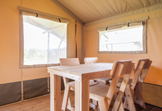 Innenansicht eines Safarizeltes mit Holztisch und Stühlen auf Camping Natürlich de Veenhoop in Friesland.