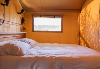 Cozy bed inside a bright safari tent at Camping Natuurlijk de Veenhoop, perfect for glamping in Friesland.