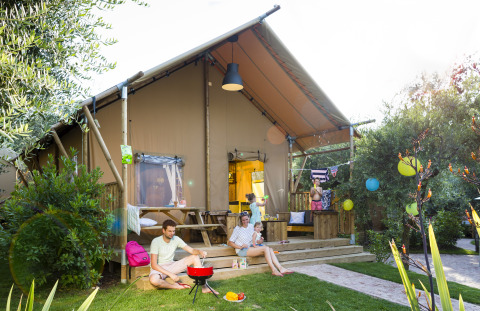 Gezin ontspant en barbequed voor een safaritent bij Weekend Glamping Resort Gardameer, omgeven door natuur.
