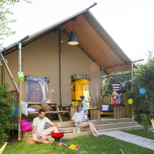 Famiglia si rilassa e fa un barbecue davanti a una tenda safari al Weekend Glamping Resort Gardameer.