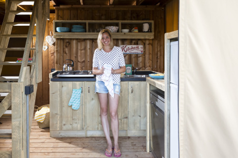 Mujer sonriente en la cocina acogedora de una tienda safari en Weekend Glamping Resort junto al Lago de Garda.