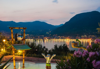 Uitzicht op Weekend Glamping Resort aan het Gardameer bij zonsondergang, met speelse figuren en bergen.