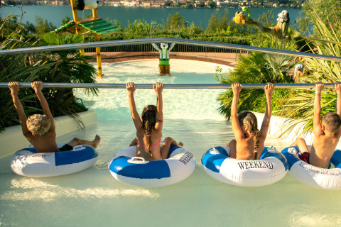 Kids sit in inflatable tubes, grabbing onto a bar at a water park in Weekend Glamping Resort at Lake Garda.