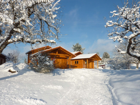Cabaña de madera entre nieve en Höhencamping Königskanzel, lodge en la Selva Negra bajo cielo azul.