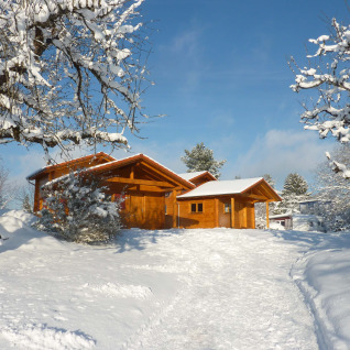 Sfeervolle houten lodge in de sneeuw bij Höhencamping Königskanzel in het Zwarte Woud, blauwe hemel.