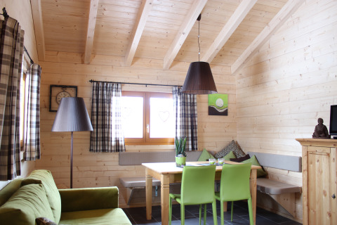 Cozy glamping lodge interior with wooden walls, green chairs, large windows and natural light in the Black Forest.