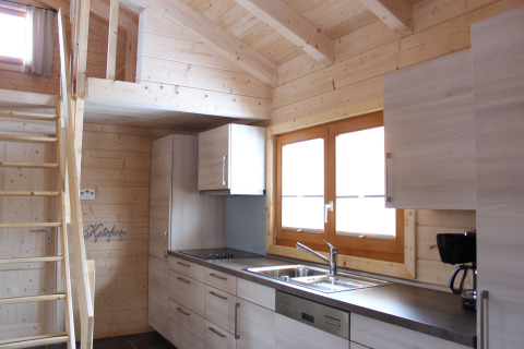 Cocina interior de una glamping lodge con paredes de madera, gabinetes modernos y altillo en Höhencamping Königskanzel.