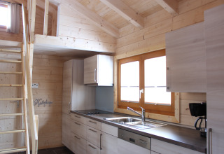 Interior of a glamping lodge kitchen with wooden walls, cabinets, windows, and loft at Höhencamping Königskanzel.