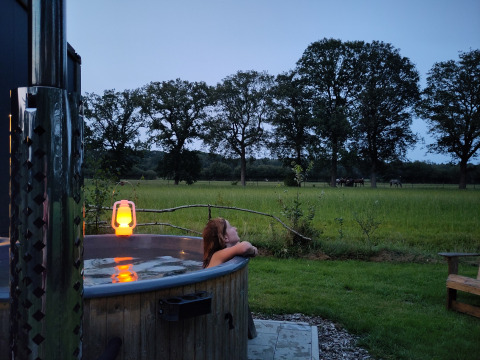 Persona disfrutando de un jacuzzi exterior al atardecer con vista a un campo verde en Uitstek - Tiny Houses Drenthe.