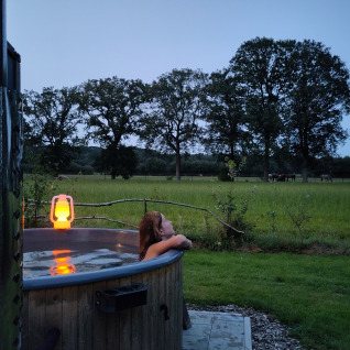Iemand geniet in een buiten bubbelbad bij valavond bij Uitstek - Tiny Houses Drenthe met zicht op een groene weide.