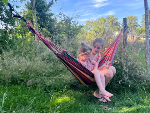 Due bambini si rilassano in un'amaca colorata sull’erba a Uitstek - Tiny Houses Drenthe glamping.