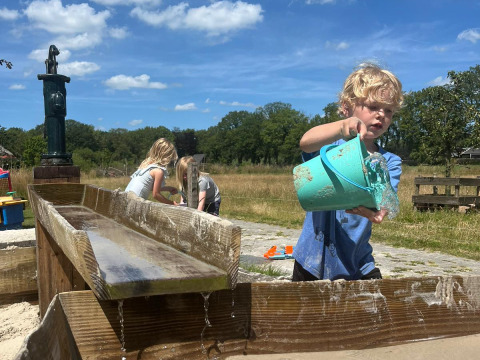 Bambini giocano con acqua e sabbia all'aperto presso Uitstek - Tiny Houses Drenthe sotto un cielo sereno.