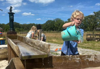 Bambini giocano con acqua e sabbia all'aperto presso Uitstek - Tiny Houses Drenthe sotto un cielo sereno.