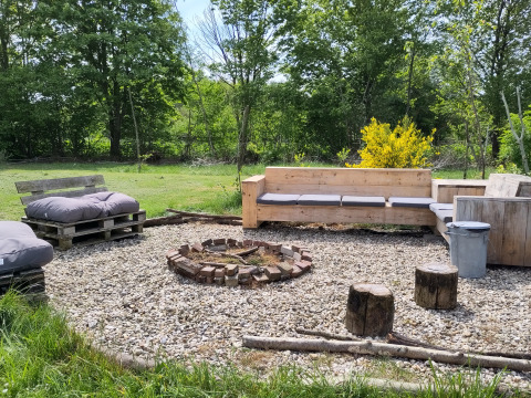 Outdoor seating area with wooden benches and fire pit at Uitstek - Tiny Houses Drenthe surrounded by trees.