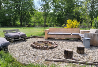 Outdoor seating area with wooden benches and fire pit at Uitstek - Tiny Houses Drenthe surrounded by trees.