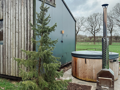 Contemporary glamping accommodation at Uitstek - Tiny Houses Drenthe, featuring a hot tub and scenic greenery.