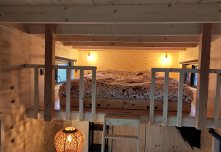Letto soppalcato con illuminazione calda e interni in legno in una glamping di Uitstek - Tiny Houses Drenthe.