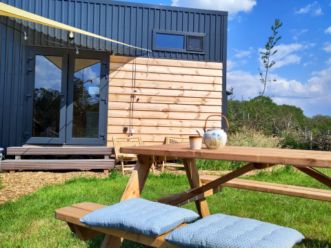 Udendørs picnicbord og bænk med puder ved siden af en moderne tiny house hos Uitstek - Tiny Houses Drenthe.