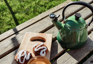 Hervidor verde, café y rollos de canela en mesa de madera en Uitstek - Tiny Houses Drenthe glamping.