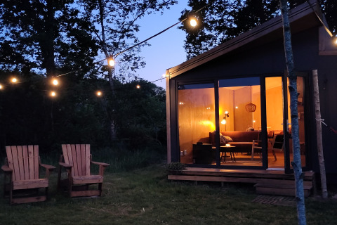 Udendørs glamping ved skumringen med to træstole, lyskæde og oplyst tiny house hos Uitstek i Drenthe.