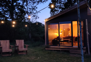 Gemütliche Glamping-Unterkunft bei Uitstek - Tiny Houses Drenthe mit Lichterkette und Holzstühlen am Abend.