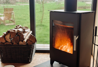 Wood stove and firewood basket inside a glamping tiny house at Uitstek - Tiny Houses Drenthe with garden view.