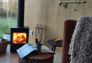 Hyggelig stue med brændeovn, kurvemøbler og stearinlys i en glamping-tiny house ved Uitstek, Drenthe.