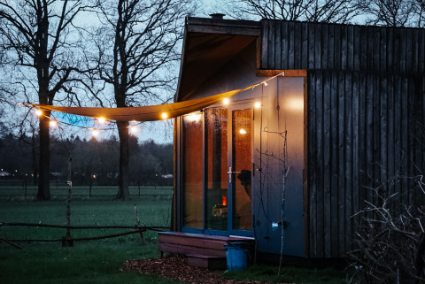 Glamping presso Uitstek - Tiny Houses Drenthe con casetta moderna, luci appese e atmosfera serena.