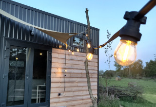 Udendørs glamping ved Uitstek - Tiny Houses Drenthe med lyskæde og moderne træbeklædt hytte.