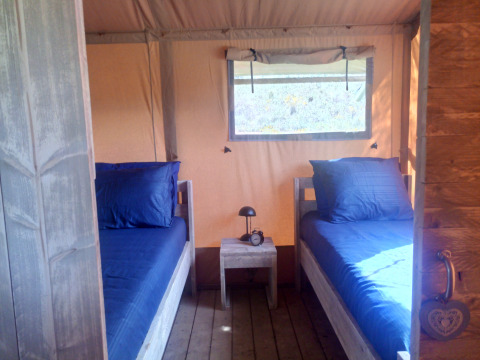 Vista interna di una tenda glamping con due letti singoli, biancheria blu e tavolino in Alentejo.