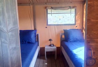 Interieur van een glampingtent met twee eenpersoonsbedden, blauwe lakens en tafel in Alentejo.