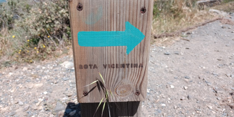 Poteau en bois avec une flèche bleue et 'Rota Vicentina', près du glamping Casa da Vinha en Alentejo.