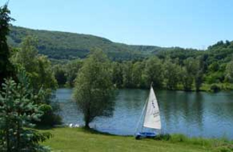 Camping Axelsee - Blokhutten Noordrijn-Westfalen met zeilboot aan vijver, tussen groene heuvels en bomen.