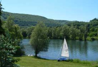 Camping Axelsee - Blokhutten i Nordrhein-Westfalen med sejlbåd ved søen, omgivet af bakker og grøn natur.