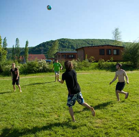 Young people play ball on a grassy field in front of cabins at Camping Axelsee, North Rhine-Westphalia.
