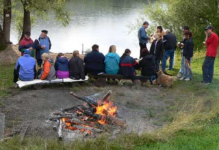 Group of people enjoying a lakeside campfire at Camping Axelsee - Blokhutten in North Rhine-Westphalia.