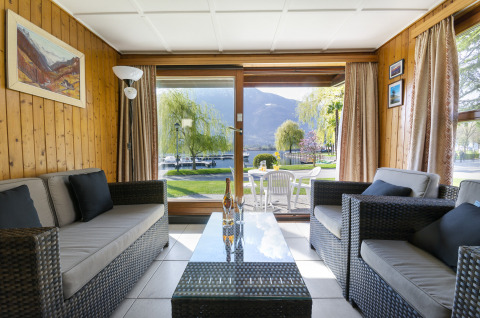 Salotto interno al Campofelice Village Camping Chalet Lago Maggiore con vista sul giardino e sul lago fuori.
