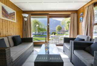Wohnbereich im Campofelice Village Camping Chalet Lago Maggiore mit Blick auf Garten und See durch Glasfront.
