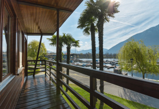 Udsigt fra en træveranda med palmer ved Campofelice Village Camping - Chalet Lago Maggiore i Schweiz.