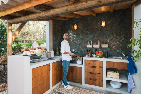 Hombre cocinando en cocina exterior con armarios de madera en Lodge Lua - Portugalvillas Glamping Algarve.