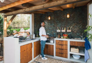 Man kookt in buitenkeuken met houten kasten bij Lodge Lua - Portugalvillas Glamping Algarve.